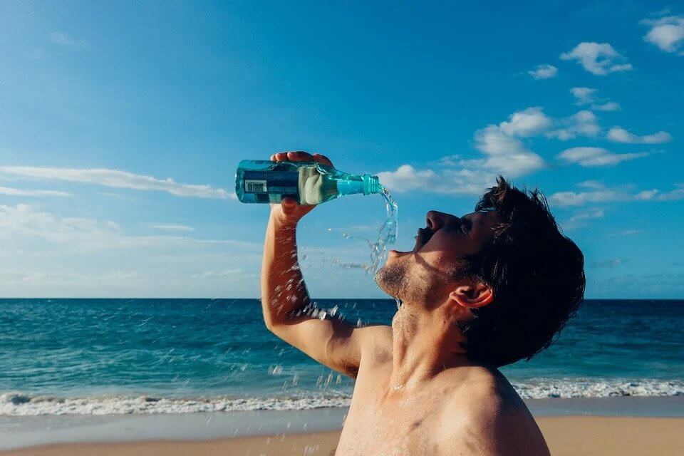 Seorang pria sedang meminum air dari dalam kemasan botol di pantai